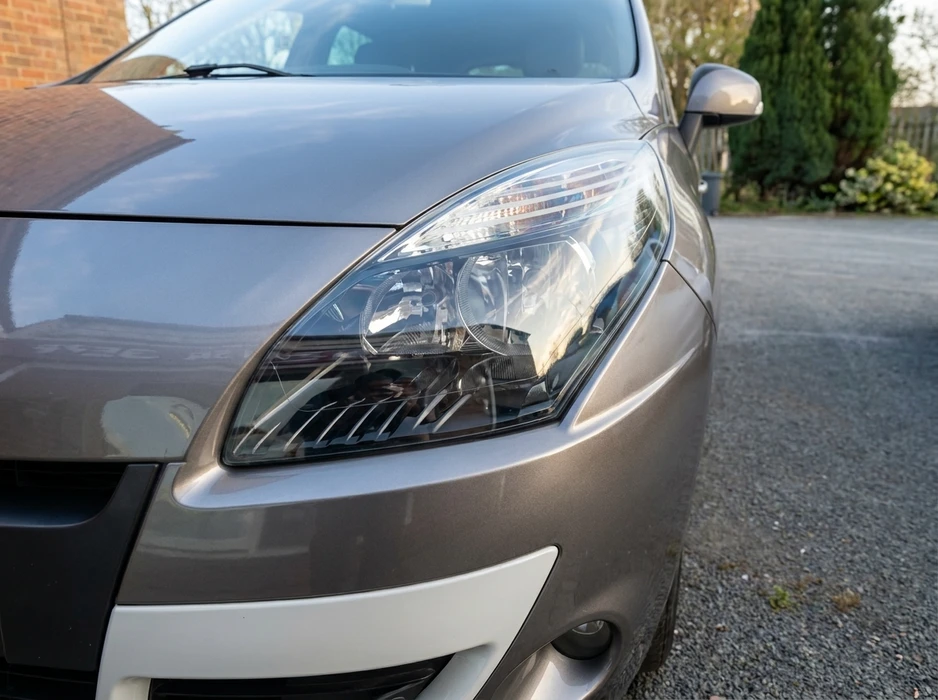 Gros plan sur l'avant d'un véhicule utilitaire compact gris taupe, garé sur une allée gravillonnée