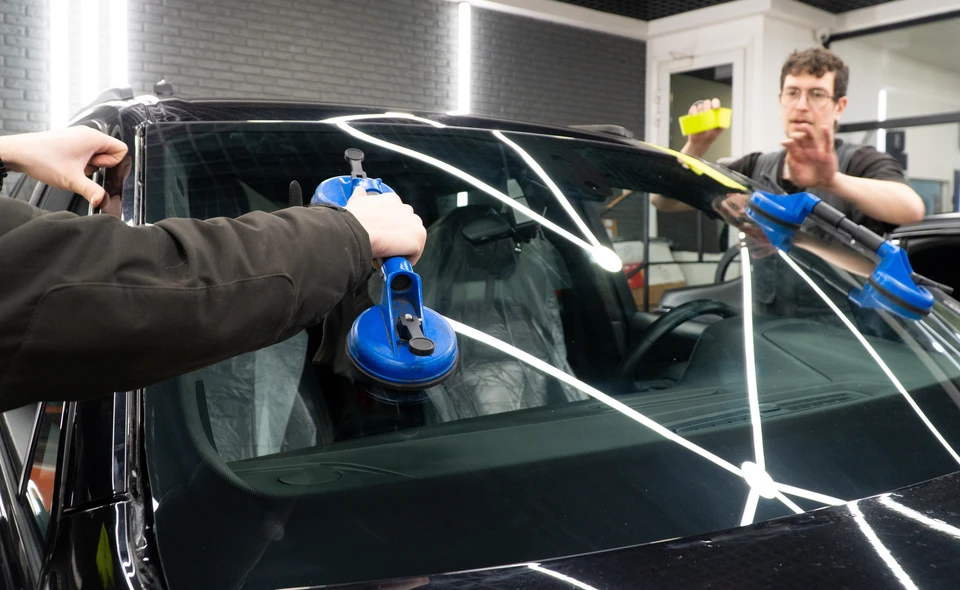 Deux techniciens installent un pare-brise automobile dans un atelier de réparation