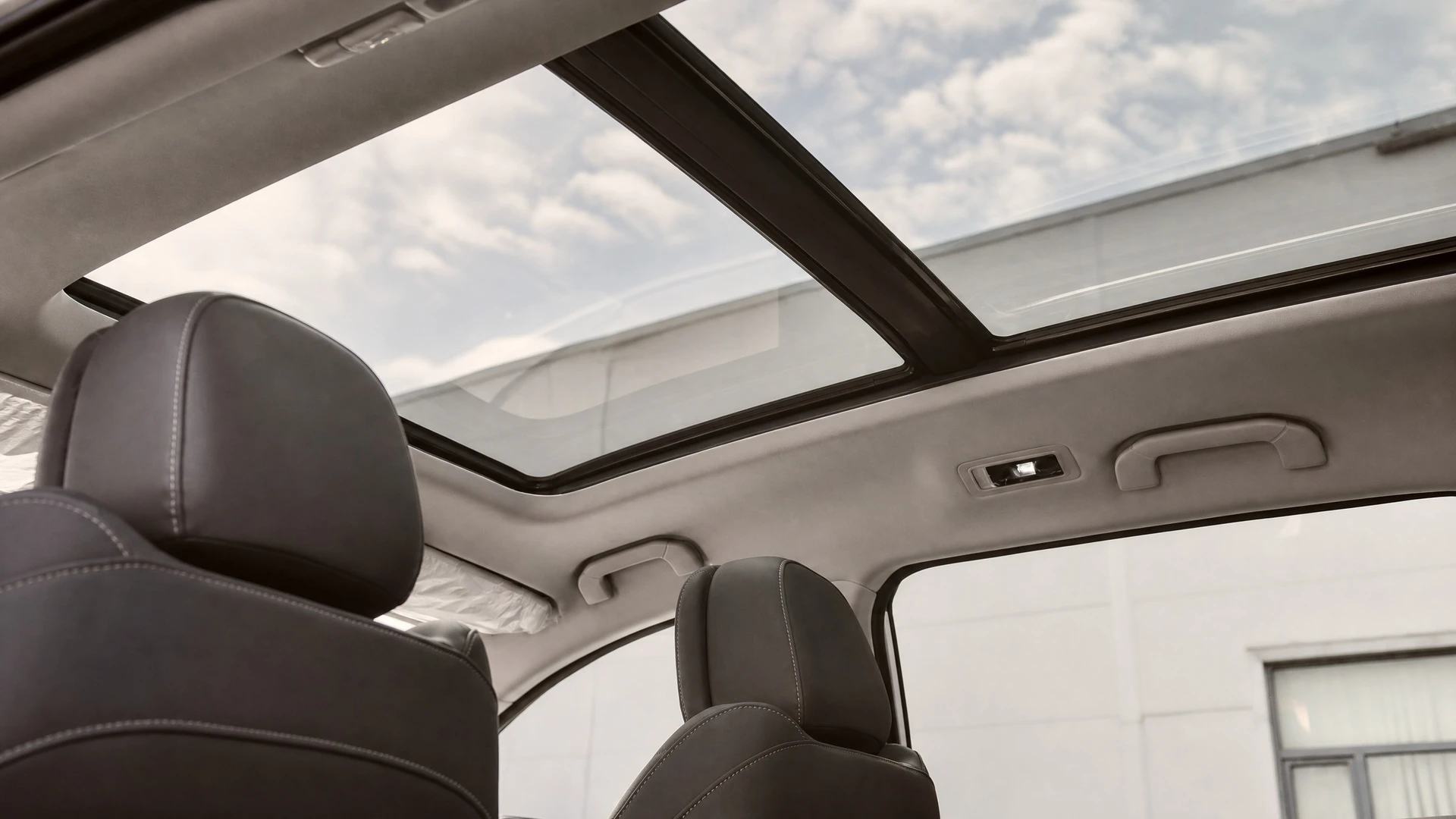Photographie d'un atelier automobile professionnel montrant un véhicule en cours de remplacement d'un toit panoramique. Le toit vitré doit être partiellement ou totalement retiré, exposant le cadre et les joints du mécanisme. Un technicien en tenue professionnelle (combinaison ou polo) effectue les opérations de dépose ou de pose du vitrage. L'environnement doit montrer un atelier bien équipé avec outillage spécialisé (ventouses de manipulation, système de retenue), sol béton, murs industriels, et éclairage professionnel. La scène doit illustrer clairement le savoir-faire et la précision du remplacement dans les règles de l'art.