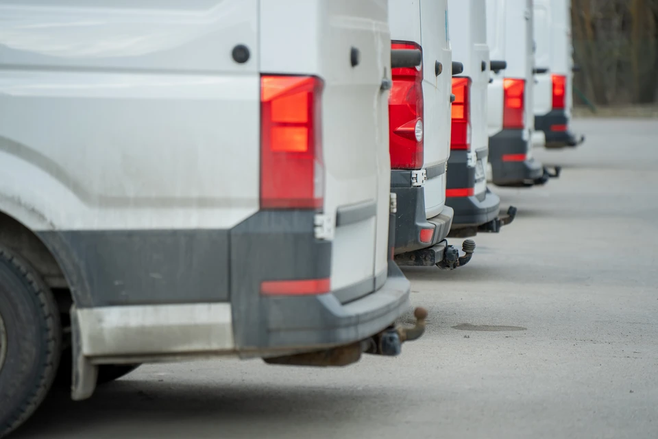 Flotte de véhicules utilitaires blancs stationnés en rangée sur parking d'entreprise avec bâtiment industriel en arrière-plan