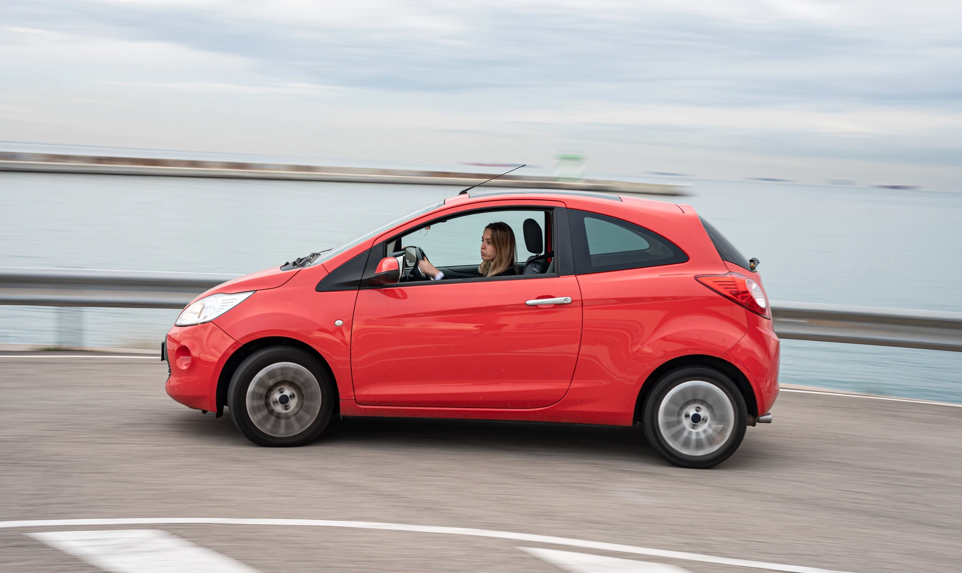 Scène extérieure urbaine montrant une voiture berline gris métallisé garée, avec feux arrière LED allumés
