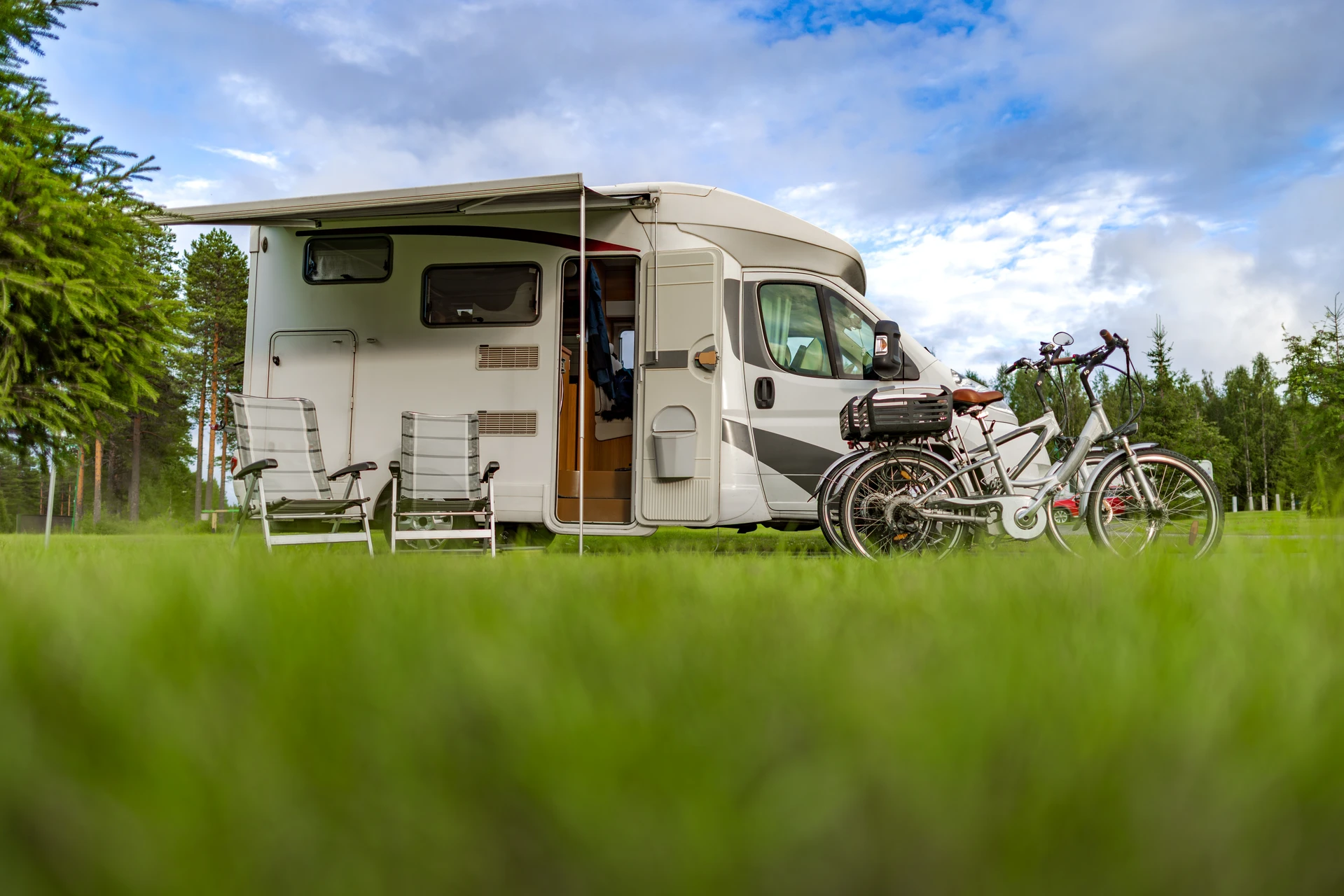 Camping-car moderne stationné en pleine nature avec deux chaises pliantes bleues disposées à l'extérieur