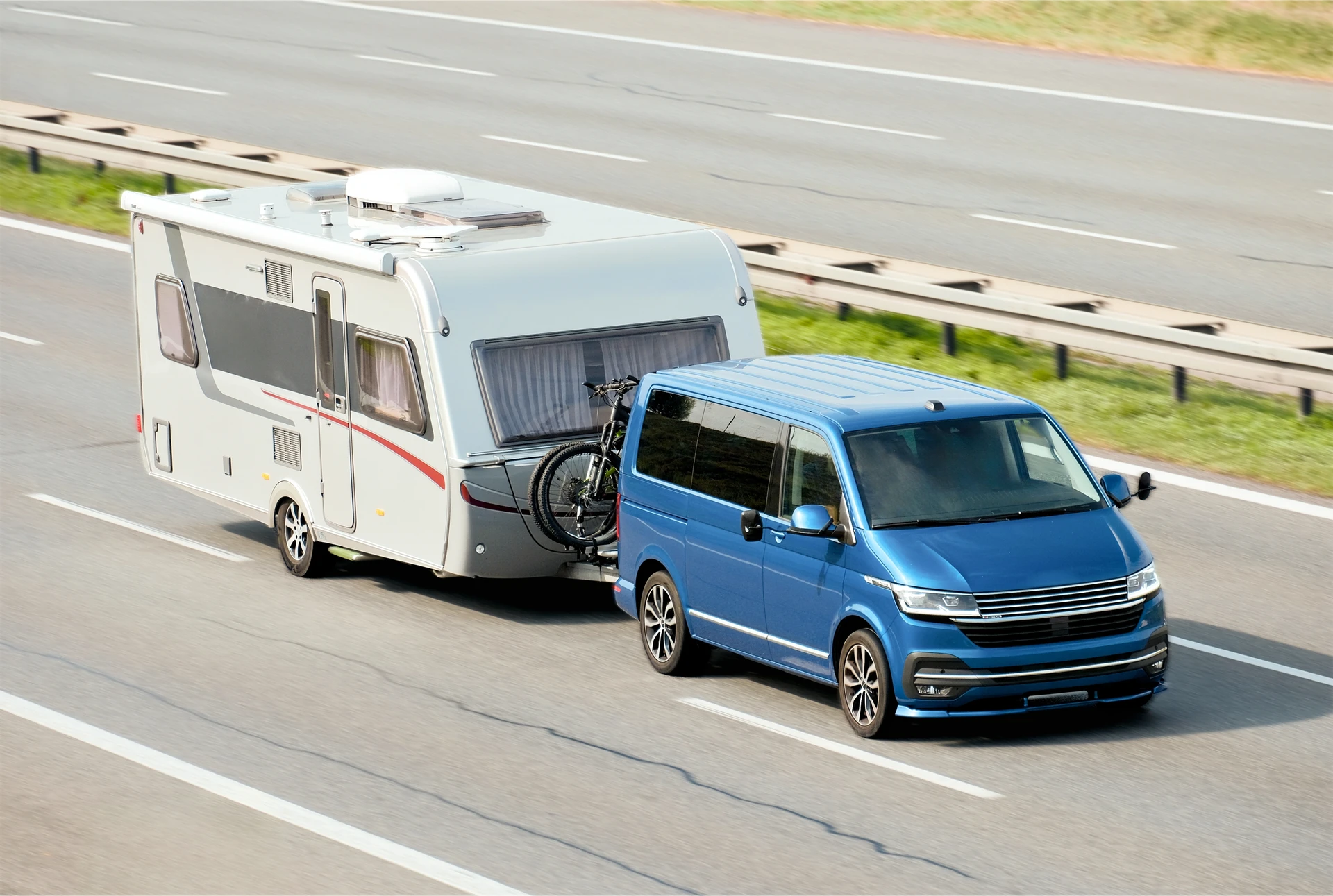 Scène extérieure avec caravane blanche et bleue tractée par SUV noir sur route goudronnée